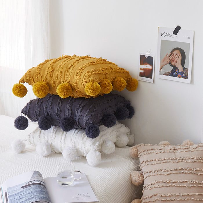 Set of decorative boho throw pillows with textured shaggy stripes and large pom-poms in mustard yellow, charcoal grey, and white for bed or sofa decor.
